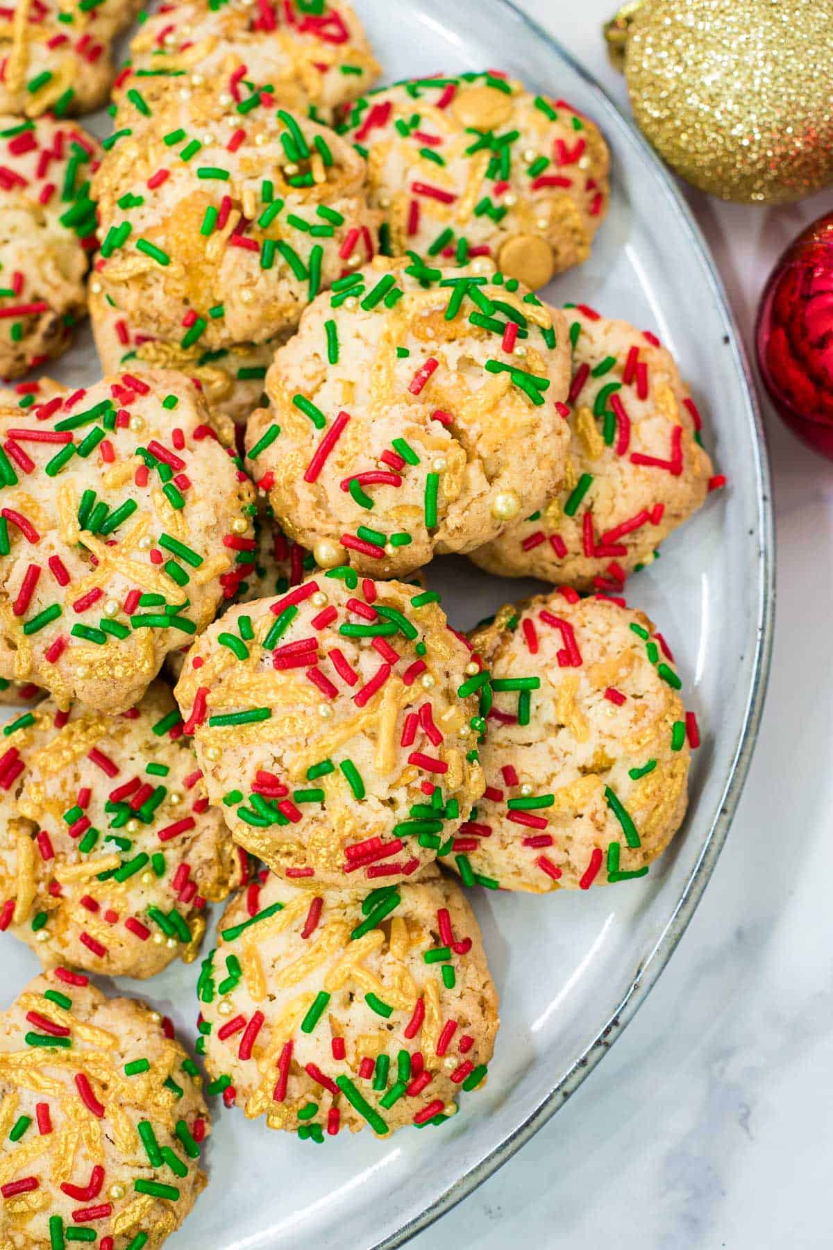 A group of cornflake cookies decorated with red, green and gold sprinkles.