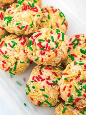 A group of cornflake cookies decorated with red, green and gold sprinkles.