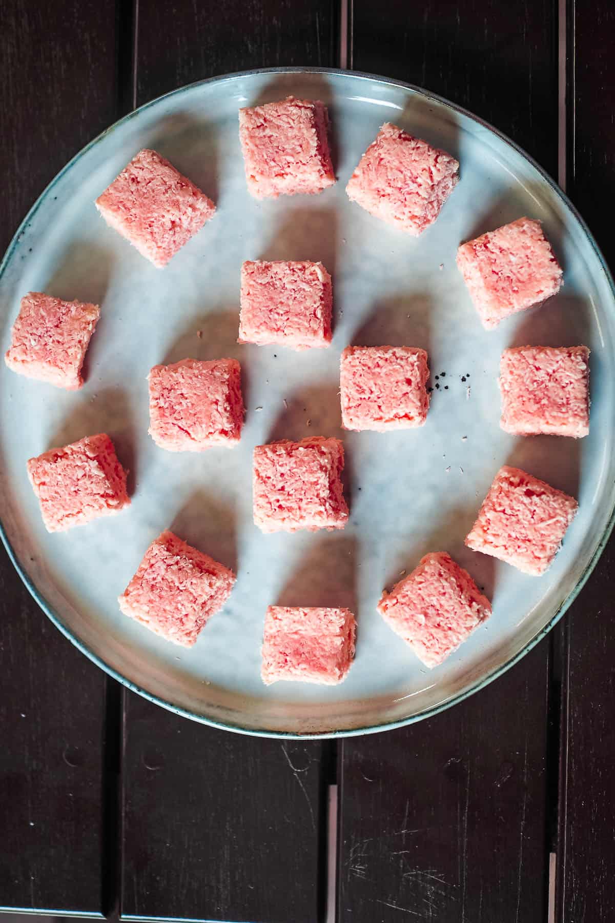 Blocks of coconut candy in pink on a white plate.