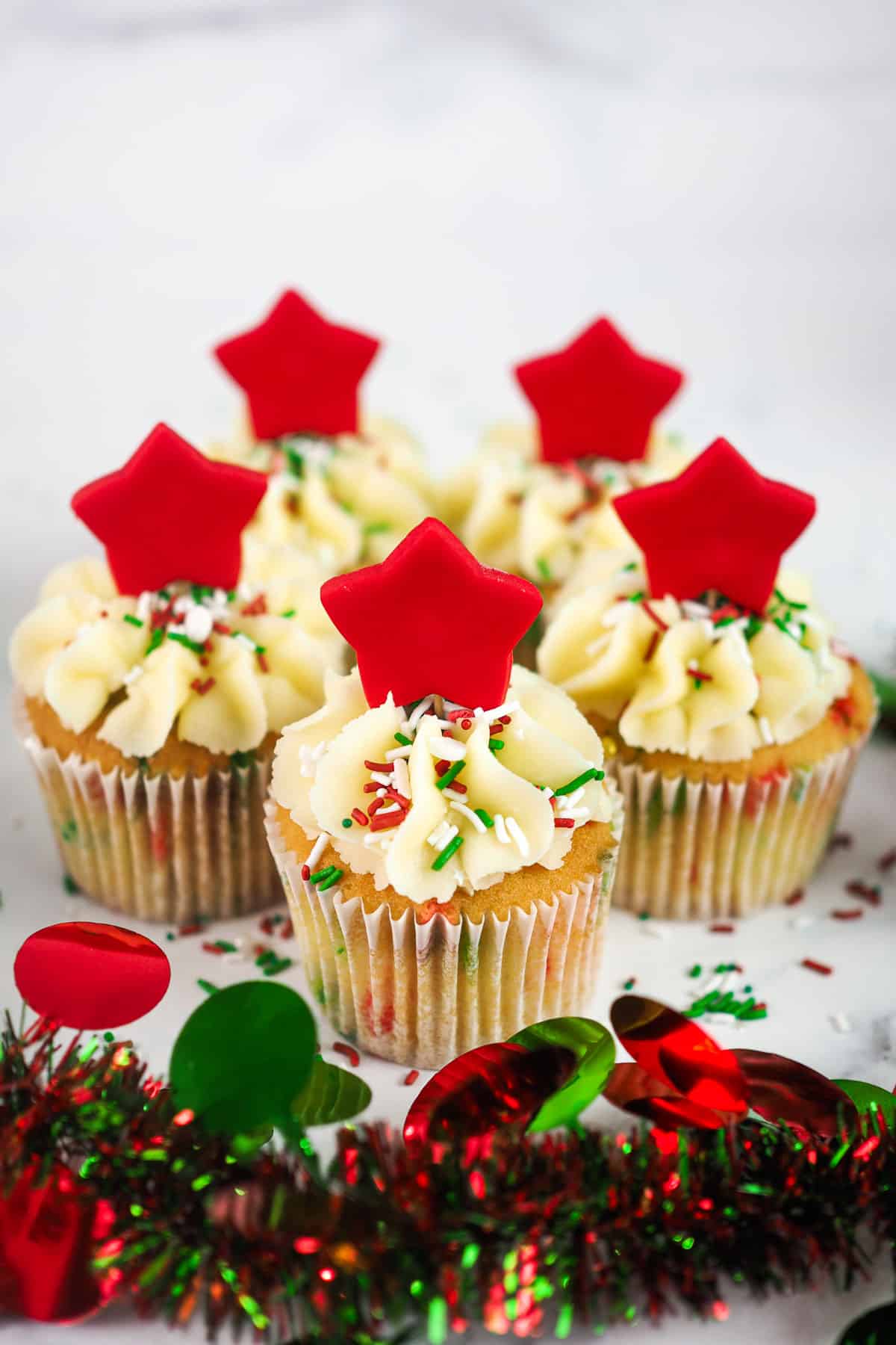 A batch of cupcakes decorated with red, white and green sprinkles and a large red fondant star.