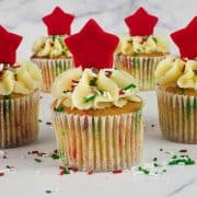 5 cupcakes decorated with red star toppers and Christmas themed sprinkles.
