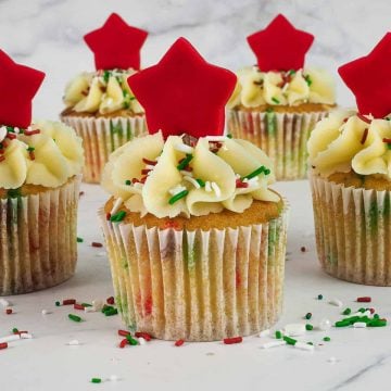 5 cupcakes decorated with red star toppers and Christmas themed sprinkles