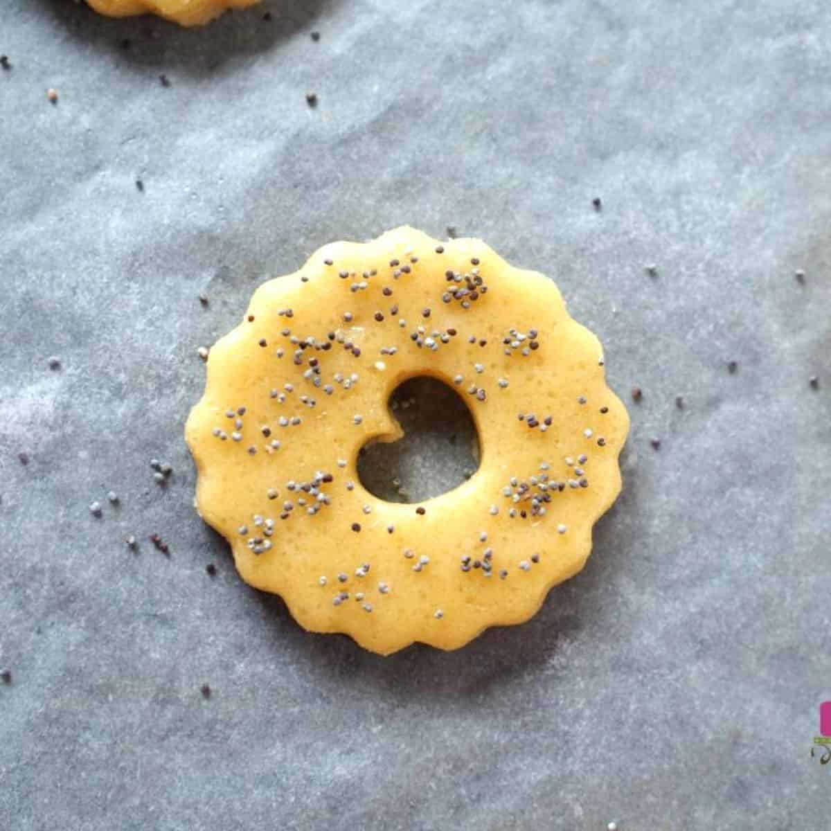 A round scalloped cookies with a heart shaped hole in the center and poppy seed garnish.