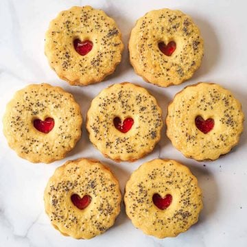 Round scalloped cookies sandwiched with strawberry jam. Cookies are with a small heart shaped hole on top