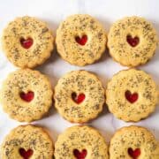 Round scalloped cookies sandwiched with strawberry jam. Cookies are with a small heart shaped hole on top
