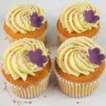 A set of 4 cupcakes in white cupcake casings decorated with buttercream, sugar sprinkles and a pretty 5 petal fondant flower.