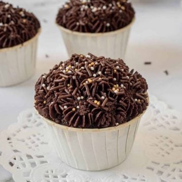 Chocolate cupcake with chocolate buttercream in white cupcake casings. Cupcakes are topped with gold and chocolate sprinkles