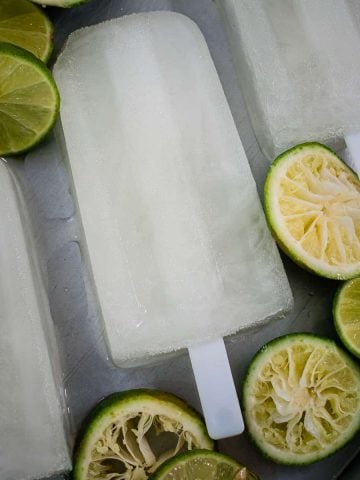 Three popsicles on a tray with sliced limes