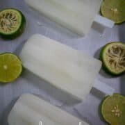 Three popsicles on a tray with sliced limes