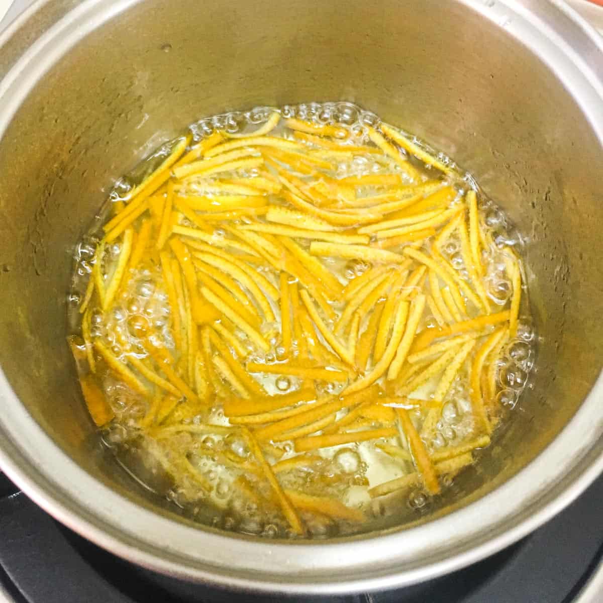 Orange peel strips simmering in a small pot.