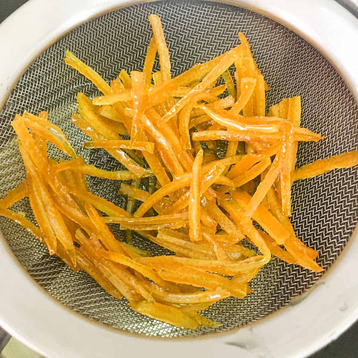 Cooked orange peel strips in a sieve.