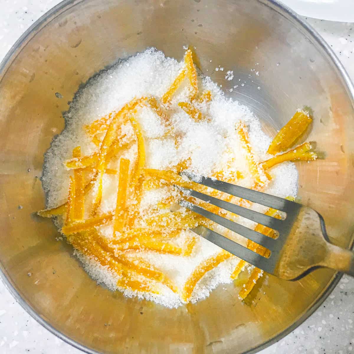 Using a fork to mix orange peel slices in a bowl of sugar