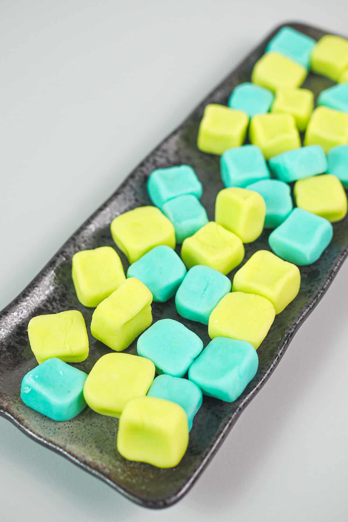 Square blue and green cream cheese mints on a rectangle brown plate.