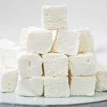 A bunch of square marshmallows stacked up on a white plate.