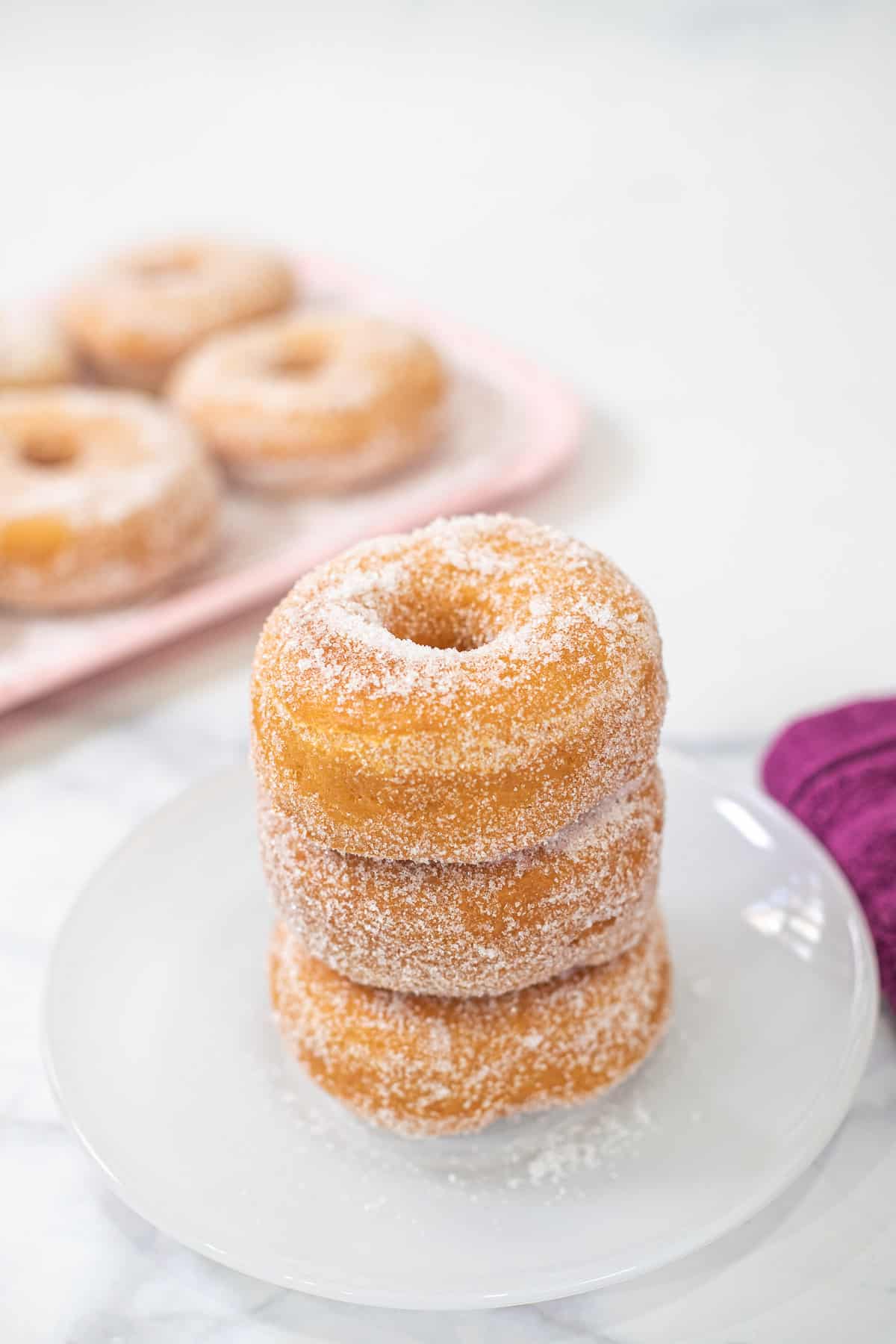 A stack of 3 doughnuts on a white plate.