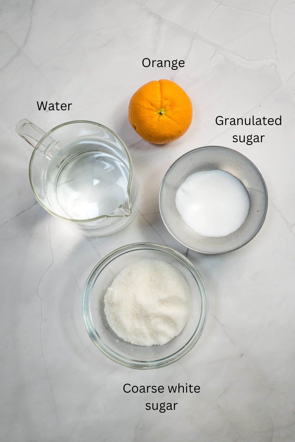An orange, a jar of water, and 2 bowls of white sugar against a marble background.