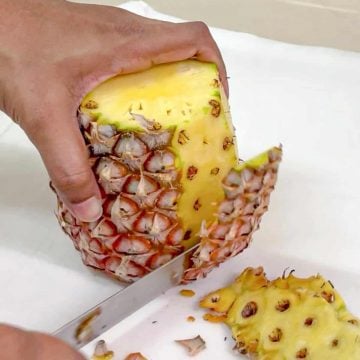A pineapple with some of its skin being cut off with a knife