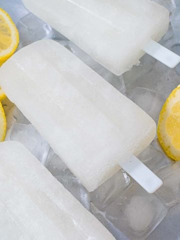 3 lemon popsicles on a tray of ice cubes and slices of lemons