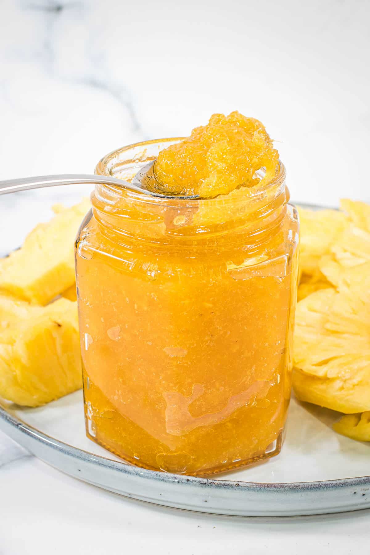 Pineapple jam in a spoon over a glass jar of jam.