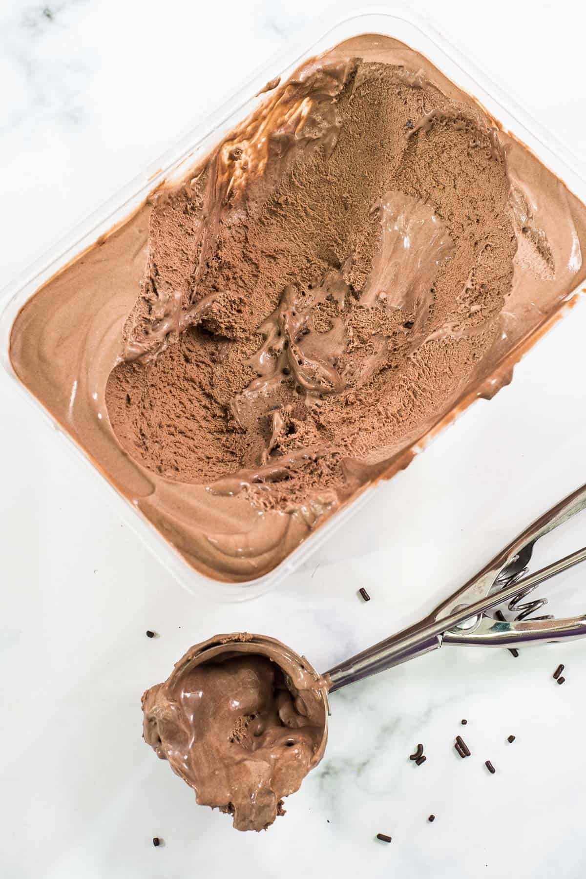 A tub of chocolate ice cream and ice cream scoop by the side