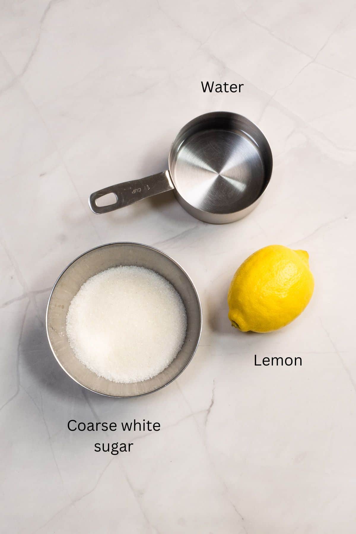 A lemon, a cup of water and a bowl of sugar against marble background.