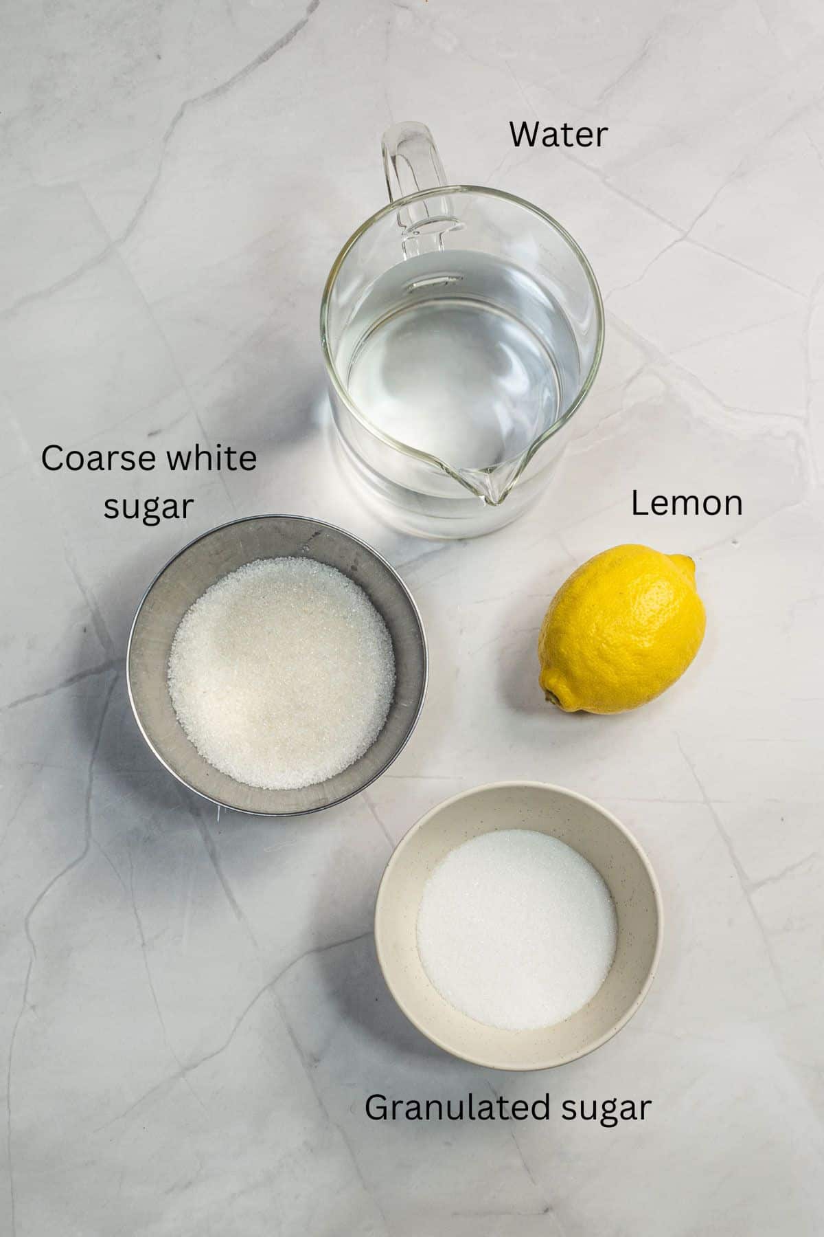 A jar of water, 2 bowls of sugar and one lemon against a marble background.