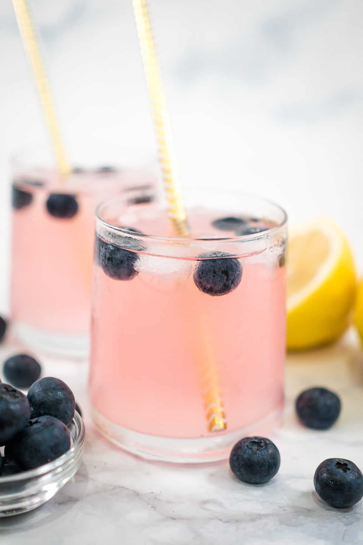 Two glasses of pink drink with blueberries and ice cubes.