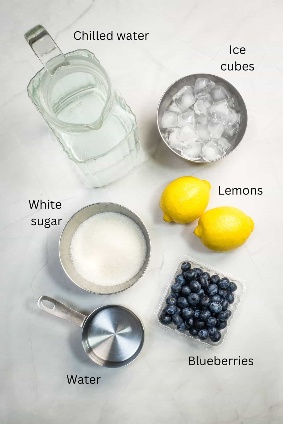 Ice cubes, sugar, water, lemons and blueberries against a marble background.