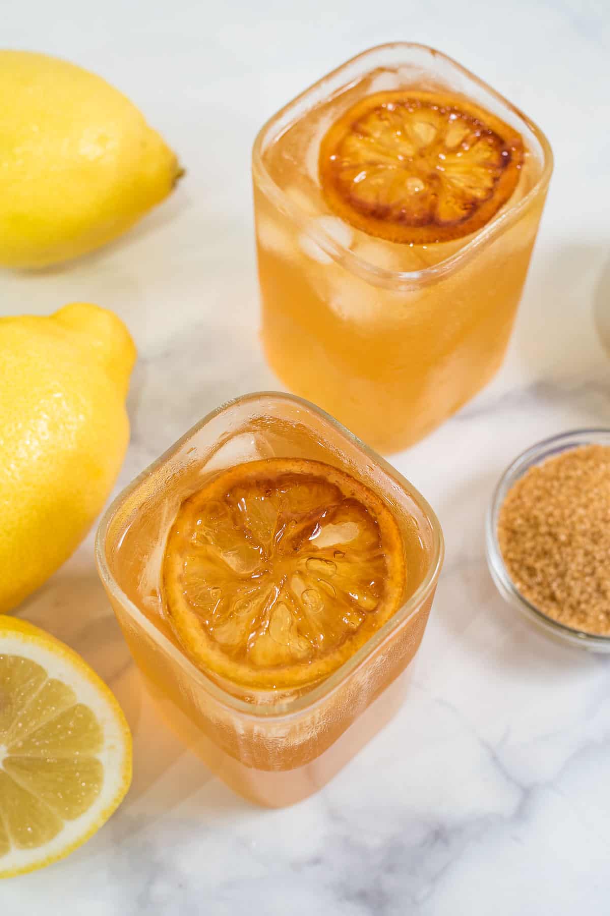 2 glasses of brown lemonade drink with caramelized lemon slices