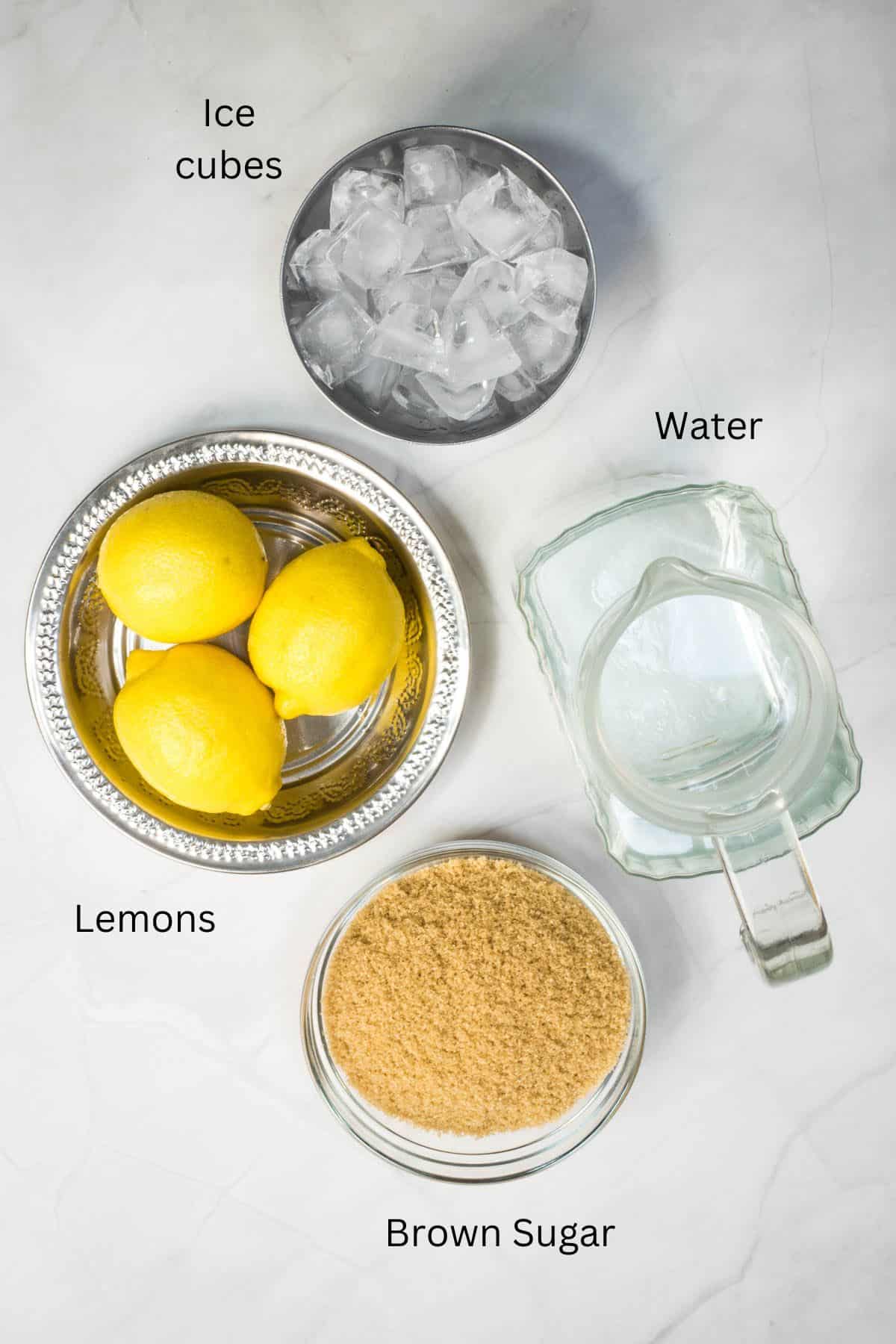 Lemons, water, ice cubes and brown sugar against a marble background.