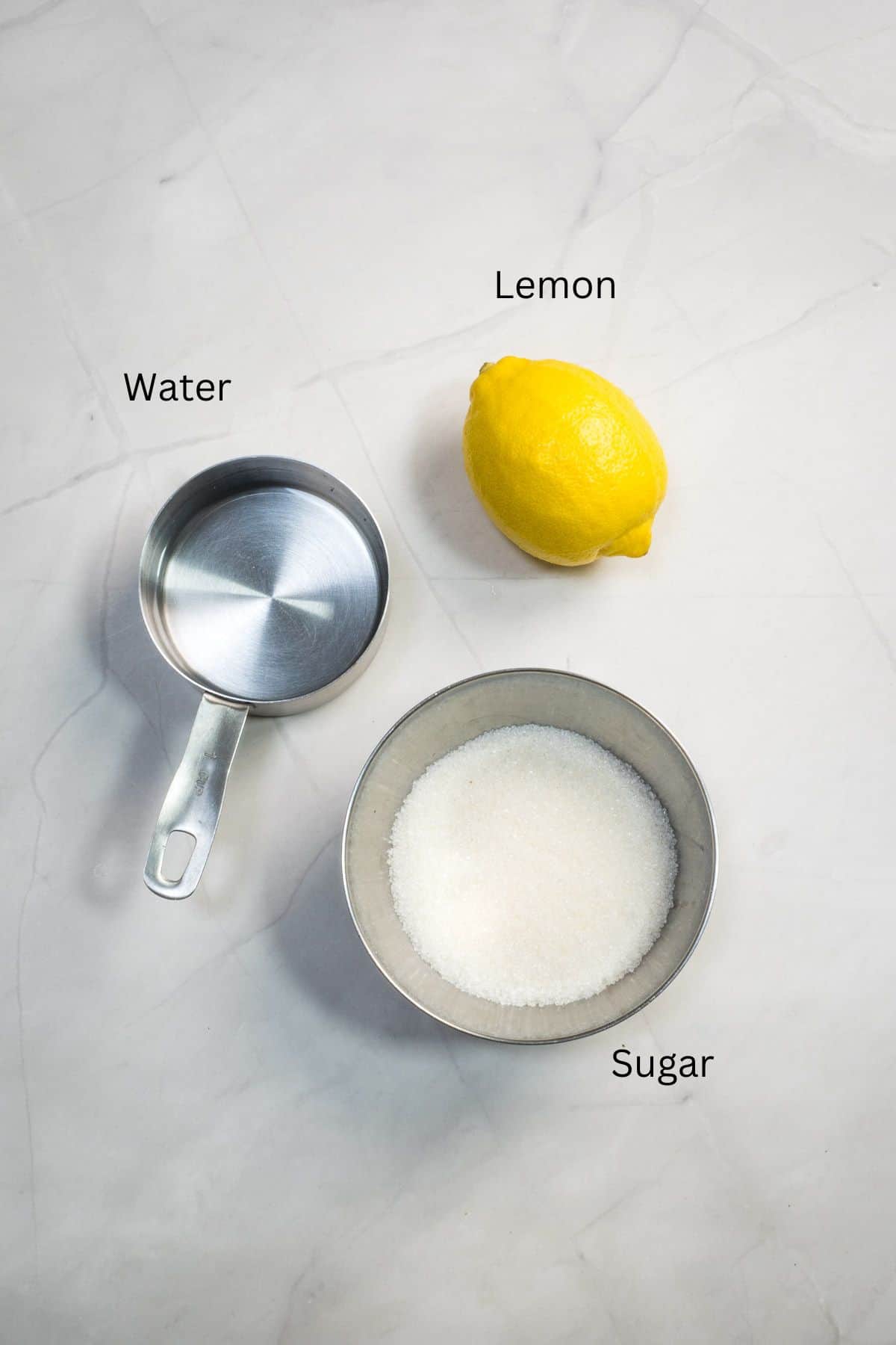 Water, sugar and a lemon against a marble background.