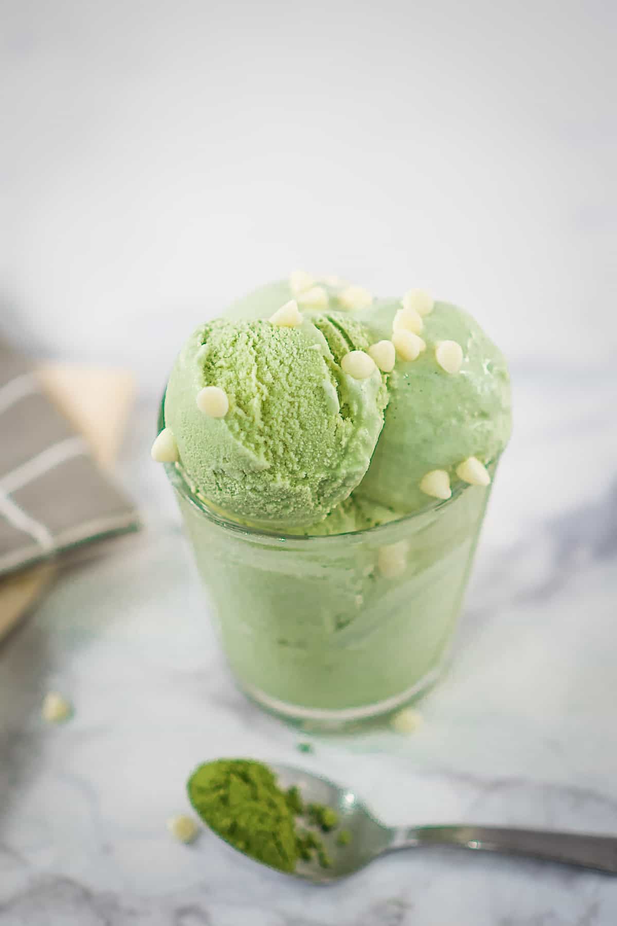 A small glass of green ice cream with while chocolate chips.