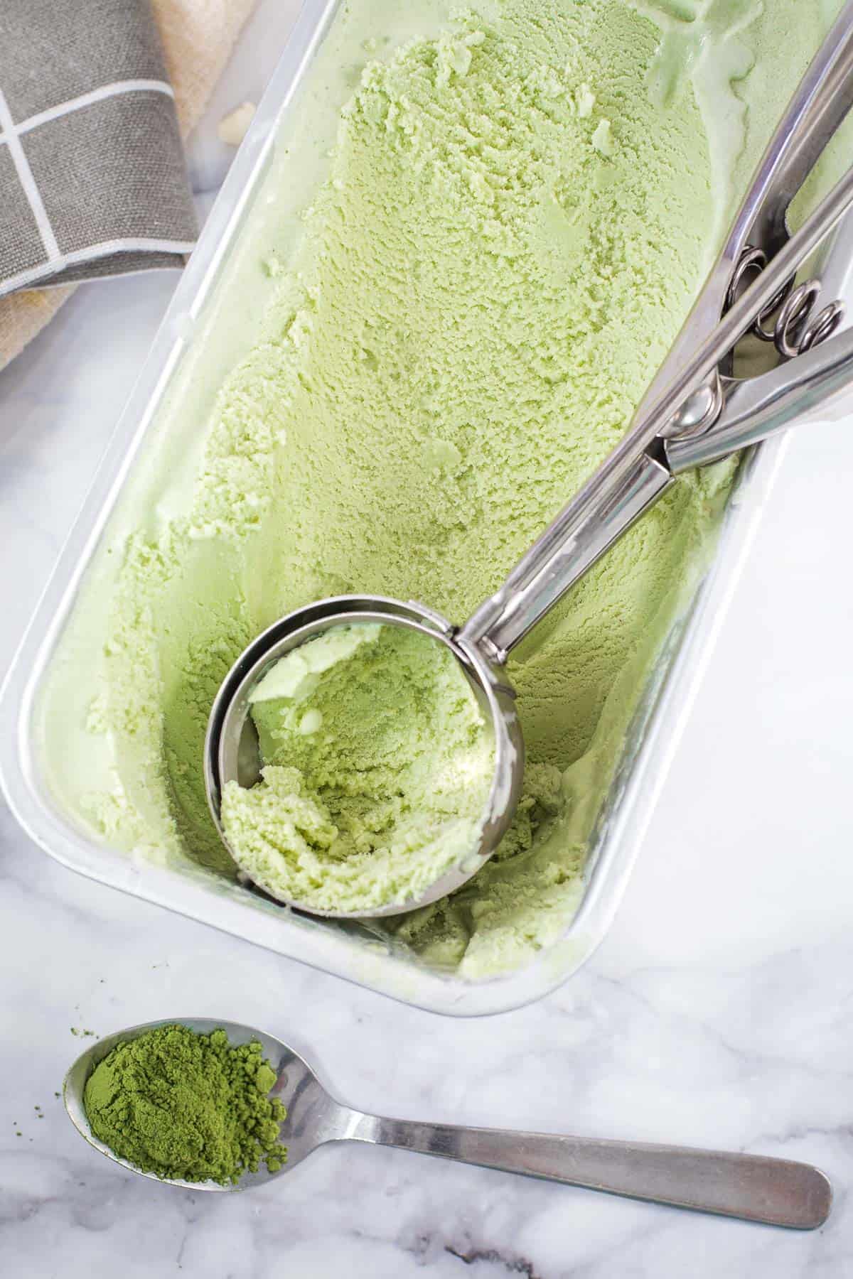 A ice cream scoop in a tub of green tea ice cream.