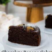 A chocolate cake on a wooden cake stand with a slice cut out onto a white plate.