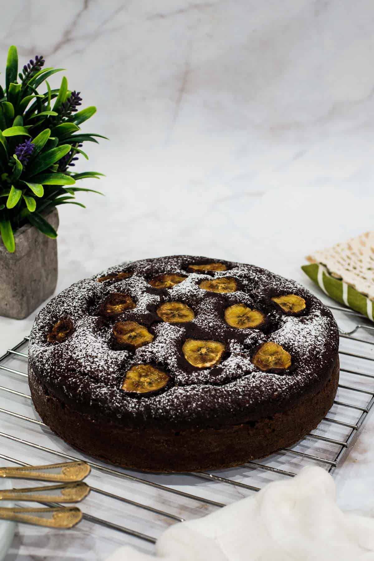 A round chocolate cake with caramelized banana slices on top, dredged with powdered sugar.
