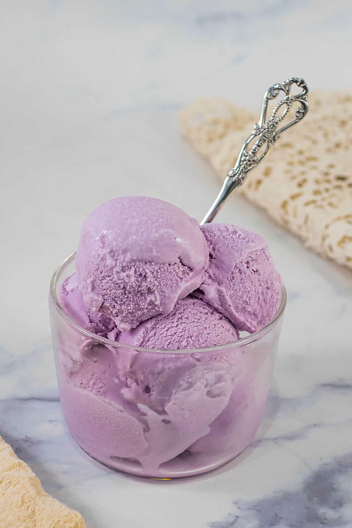 Scoops of purple ice cream in a transparent glass with a silver spoon
