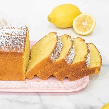 A loaf of sour cream lemon cake cut into slices on a pink tray