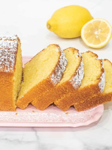 A loaf of sour cream lemon cake cut into slices on a pink tray.