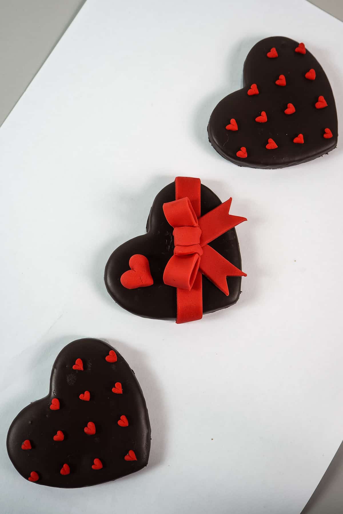 A set of 3 heart shaped cookies decorated with red hearts and bow