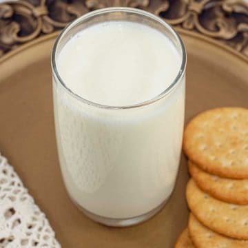 A glass of milk on a brown tray with cookies on the side