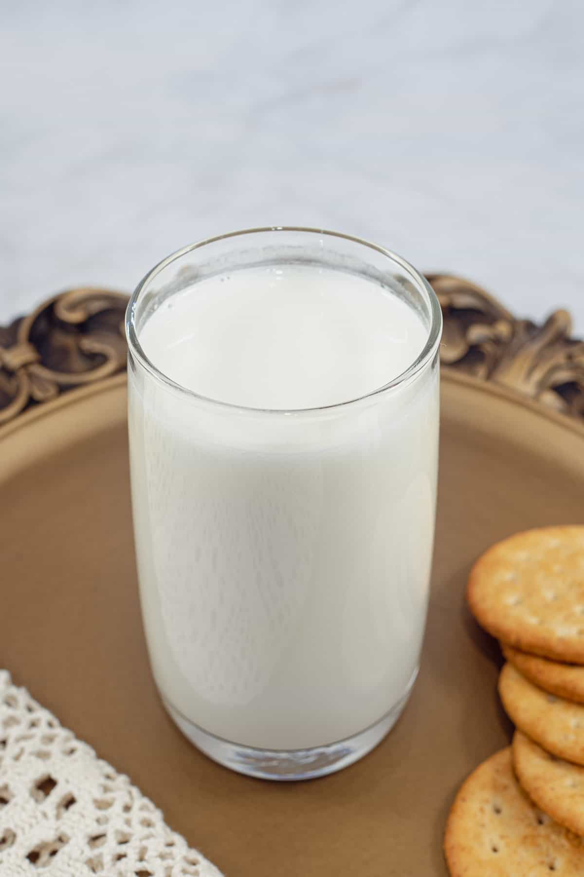 A glass of milk on a brown tray with cookies on the side.