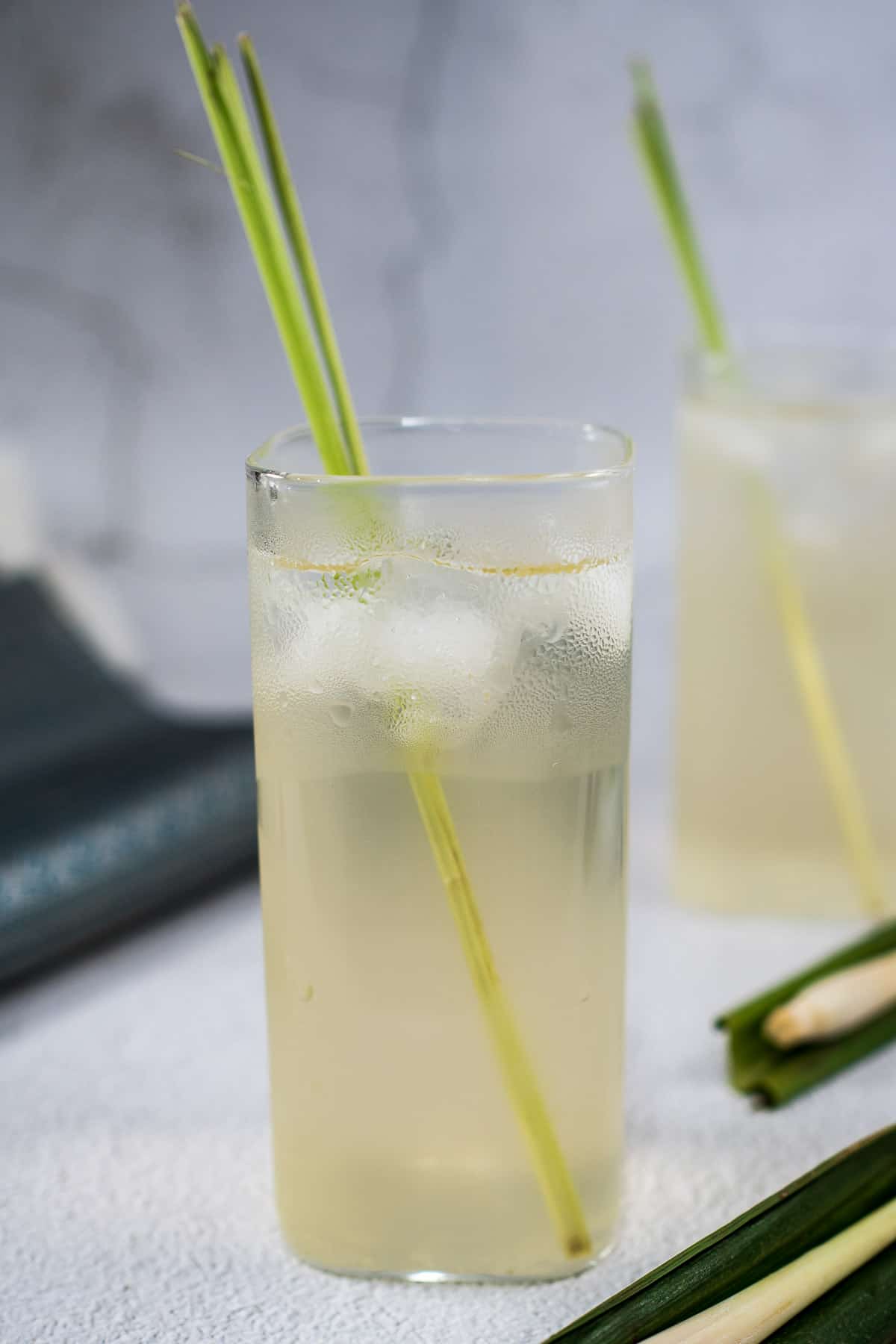 2 glasses of iced lemongrass pandan tea with lemongrass stalks garnish.