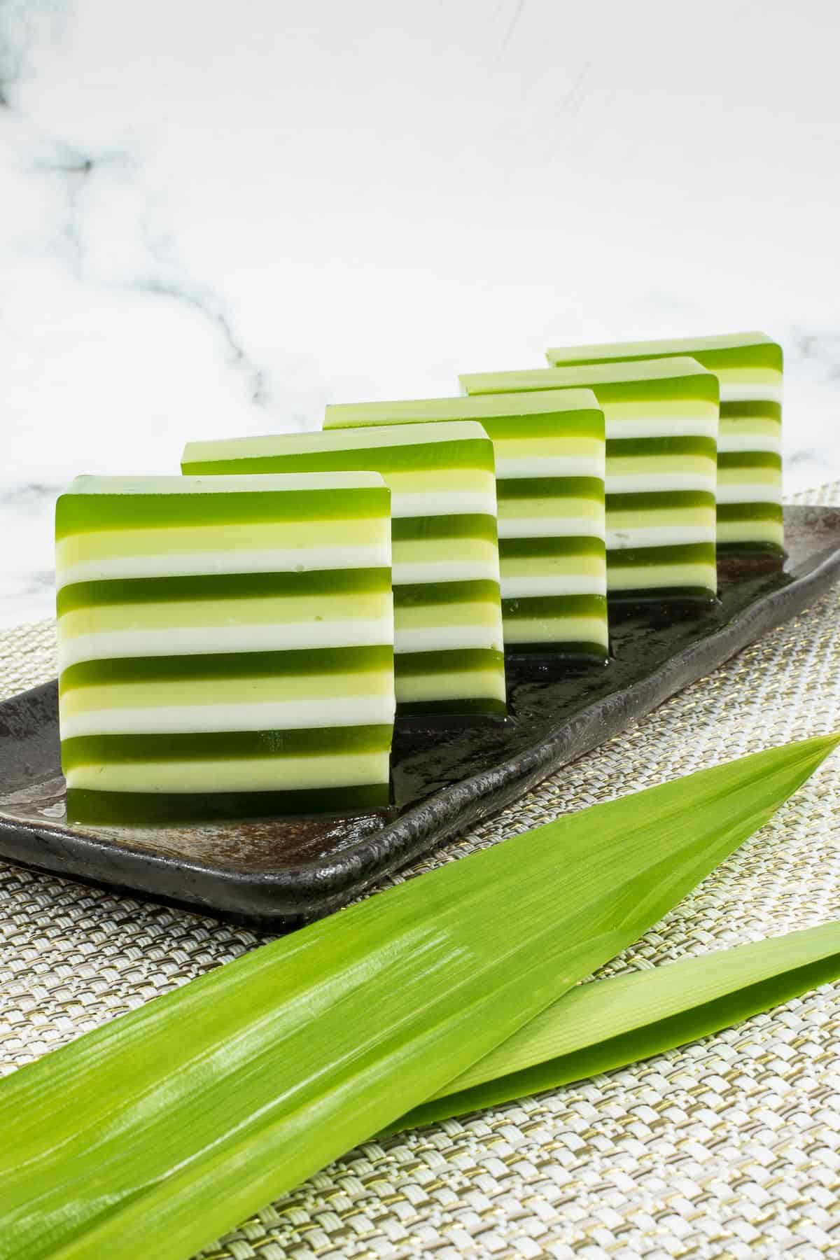 Green and white layered jelly cut into pieces and arranged on a brown rectangle plate.