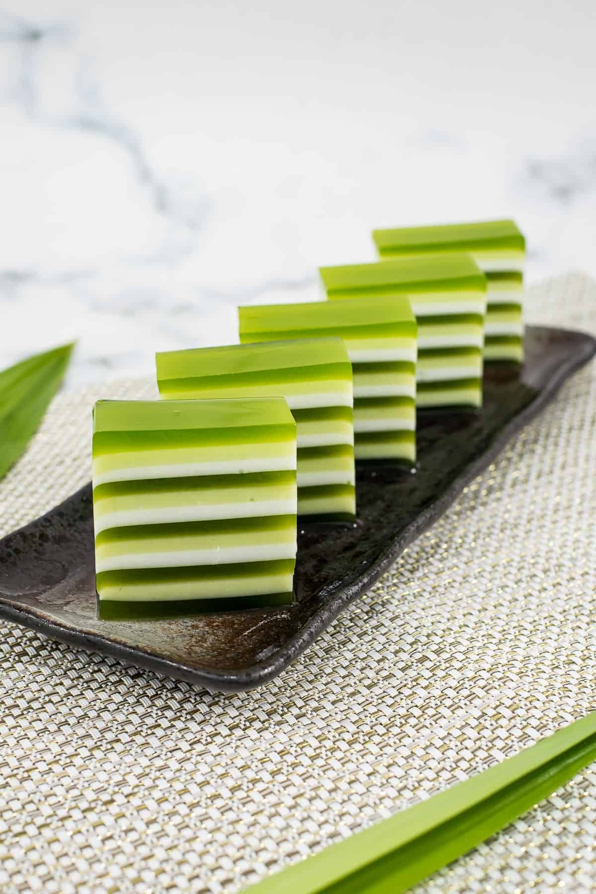 Green and white layered jelly cut into pieces and arranged on a brown rectangle plate.