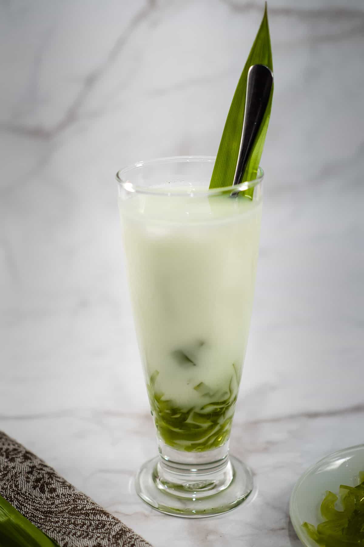 A tall glass of milk with green jelly boba strips.