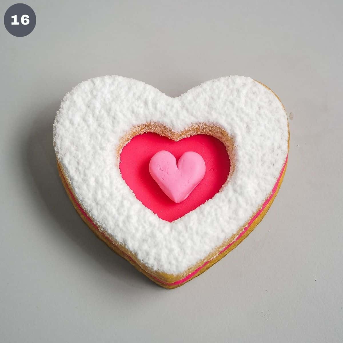A heart cookie with pink fondant heart center and powdered sugar topping.