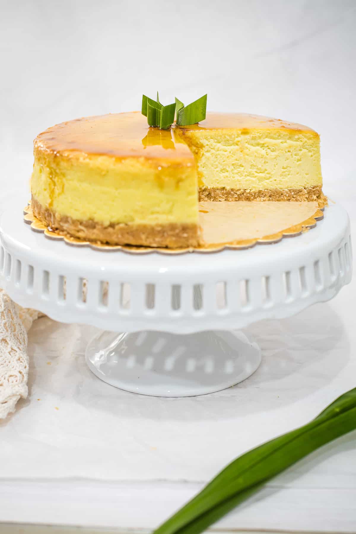 A round pandan cheesecake with gula melaka syrup, with a slice cut out.