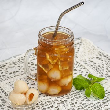 A glass of black lychee tea with real lychee fruits.