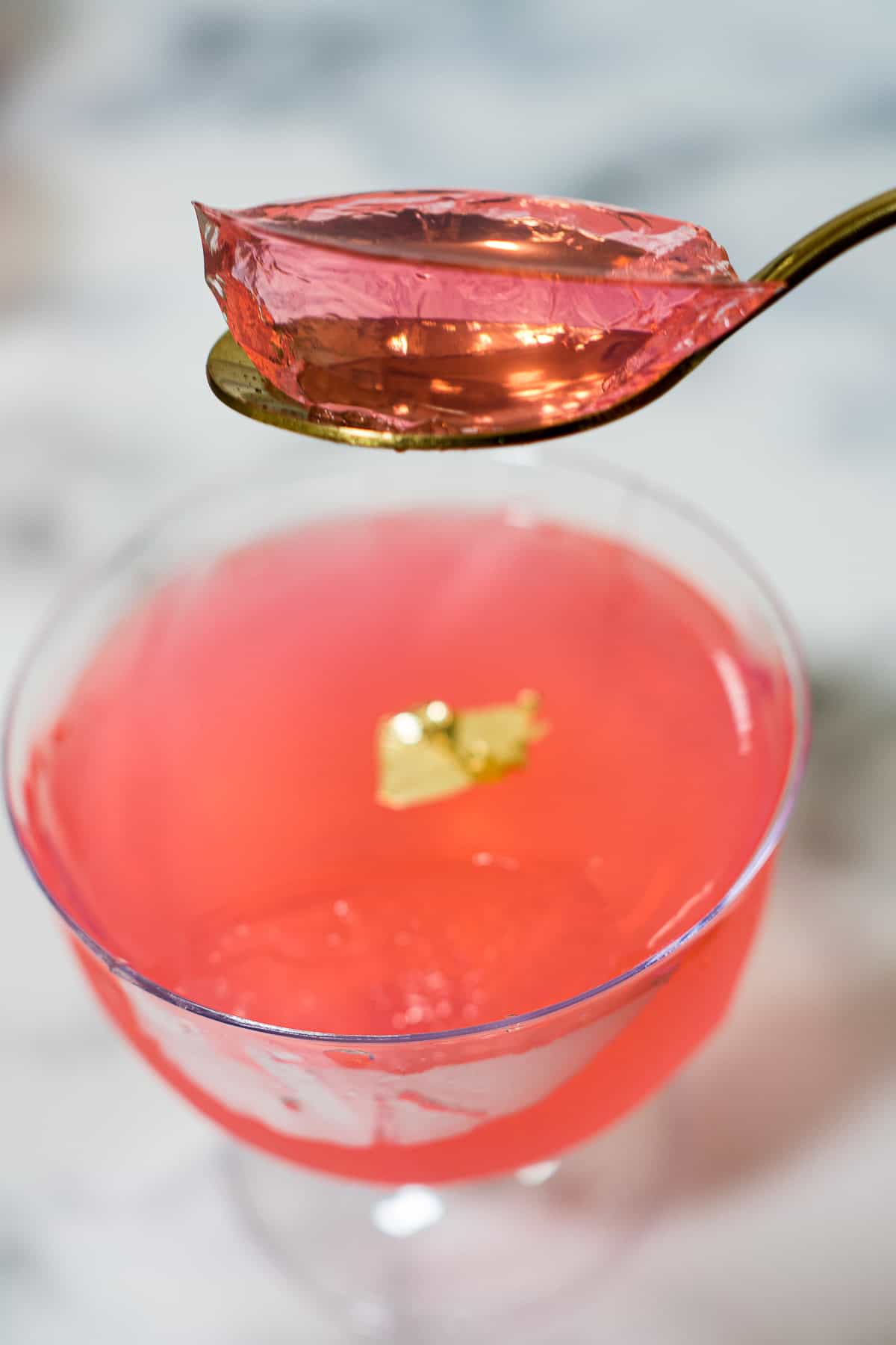 A scoop of pink jelly in a gold spoon.