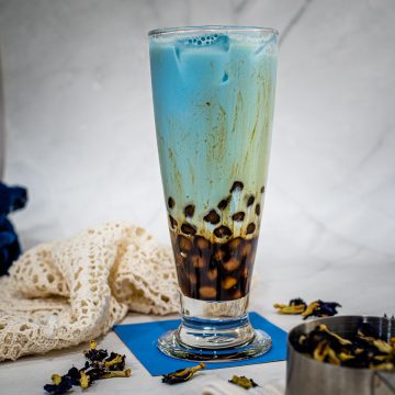 A tall glass of blue milk tea and brown sugar tapioca pearls.